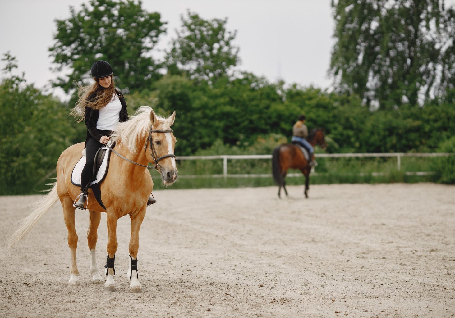 Rider woman riding her horse on a ranch. Woman has long hair and black clothes. Blurred second rider on a horse on a background.